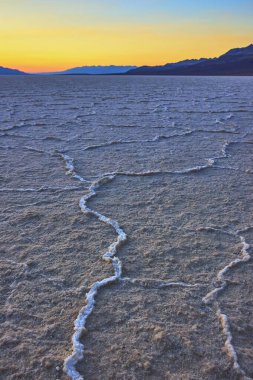 Nevada Ölüm Vadisi 'ndeki Badwater Havzası boyunca uzanan tuzlu kabuk desenleri uzak dağların ardında parlayan altın saat gökyüzü dingin ve dünya dışı bir çöl manzarası yaratıyor..