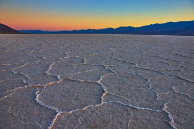 Nevada Ölüm Vadisi 'ndeki Badwater Havzası boyunca uzanan çarpıcı geometrik desenli tuzlu düzlükler altın saat ışığı ve uzak dağlar sakin ve dramatik bir çöl manzarası yaratıyor..