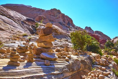 Yığılmış cairns ve kaya oluşumları Kızıl Kaya Kanyonu Nevada 'daki Calico Tank Patikası' nda çöl bitkileri ve engebeli kumtaşlarıyla dolu canlı mavi gökyüzü altında çarpıcı bir doğal manzara yaratıyor..