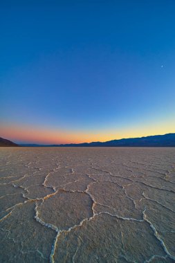 Nevada Ölüm Vadisi 'ndeki Badwater Havzası' nın tuzlu düzlükleri, engebeli dağ siluetleri ve dramatik bir çöl manzarası yaratan uçsuz bucaksız bir gökyüzü ile altın saat ışığı altında parıldıyor..