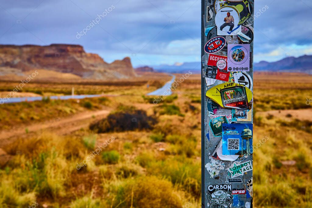 A colorful sticker-covered Welcome to Utah sign stands along a winding desert highway near Big Water with dramatic mesas in the background inviting travelers to explore the American Southwest
