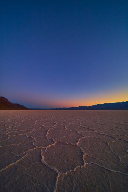 Nevada Ölüm Vadisi 'ndeki Badwater Havzası' nın dokulu tuz düzlükleri uzak dağların çarpıcı ve sakin çöl manzarası oluşturduğu canlı bir alacakaranlık gökyüzünün altında uzanıyor..