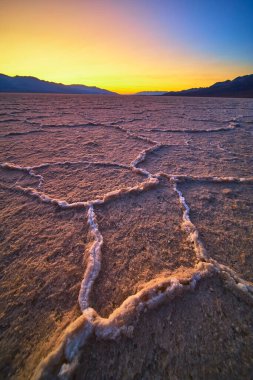 Ölüm Vadisi 'ndeki Badwater Havzası' nın karmaşık tuz çokgenleri Nevada 'nın uzak dağları dramatik ve sakin bir manzara yaratırken canlı bir altın saat gökyüzünün altında parlıyor..