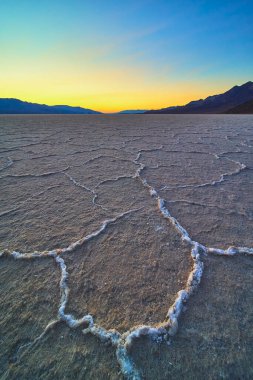 Tuz tabakası oluşumları Badwater Havzası boyunca uzanır Ölüm Vadisi Nevada 'da altın saat ve uzak dağlar ve canlı bir gökyüzü huzurlu ve dramatik çöl manzarası yaratır..