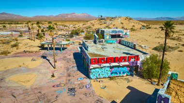 Kaliforniya 'da terk edilmiş bir su parkının gökyüzü manzarası. Grafiti kaplı binalar, palmiye ağaçları ve açık mavi gökyüzünün altındaki kurak çöl manzarası..