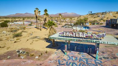 California 'daki terk edilmiş Dolores Gölü su parkının hava manzarası graffiti kaplı yapıları, canlı palmiyeleri ve parlak mavi gökyüzünün altındaki geniş çöl ortamını gösteriyor..