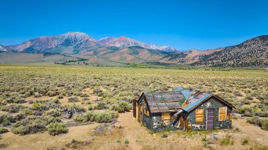 Lee Vining California 'da terk edilmiş bir evin havadan görünüşü. Williams Butte ve engebeli dağ manzarası açık mavi gökyüzü altında..