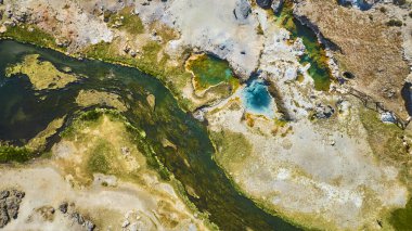 Mamut Gölleri yakınlarındaki Hot Creek Jeolojik Alanı 'nın havadan görünüşü dolambaçlı bir nehir ve parlak güneş ışığında mineral zengini arazilerle çevrili canlı jeotermal havuzlar gösteriyor..
