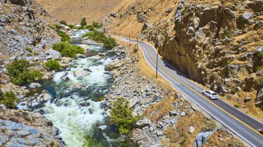 Kern Nehri 'nin Sequoia Ulusal Ormanı' ndaki dolambaçlı bir yolun kenarındaki kayalık arazide uzanan hava manzaralı manzarası. Parlak yaz güneşi altında manzaralı yol boyunca bir araba seyahat ediyor..