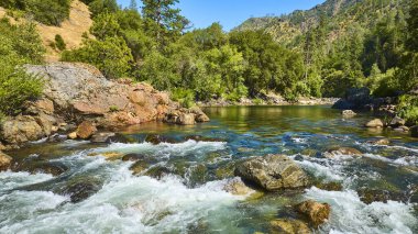 Merced Nehri 'nin berrak suları, yoğun yeşil ormanlar ve Kaliforniya' nın engebeli tepeleri arasında kayaların üzerinde çağlayarak canlı ve ferahlatıcı bir açık hava manzarası yaratır..