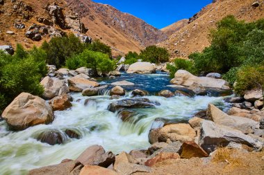 Kern Nehri 'ndeki granit kayaların üzerinden akan sular Sequoia Ulusal Ormanı' ndaki yemyeşil ve kurak dağlarla çevrili parlak mavi gökyüzünün altında..