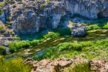 Güneşli bir nehir California 'daki Hot Creek Jeolojik Alanı' ndan geçiyor. Mamut Gölleri 'nin yakınındaki kayalık uçurumlar ve jeotermal yeşilliklerle çevrili..