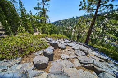 Kaliforniya 'daki Devils Postpile' deki belirgin bazalt kaya oluşumları gür çam ormanlarıyla çevrili ve berrak bir yaz gökyüzünün altındaki manzaralı dağ vadisine bakan.