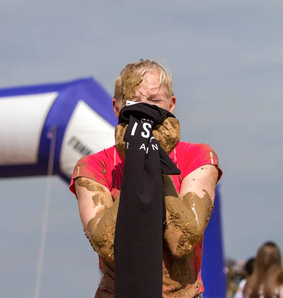 The girl puts a T-shirt on her face, with an inscription Finisher on the background of the arch of the finish of a public race with obstacles. The inscription Finish on the arch is written in Ukrainian.