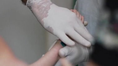 Doktorun ellerinin yakın çekiminde yaralı çocuğun sağ bacağını tutarak. ses yok.