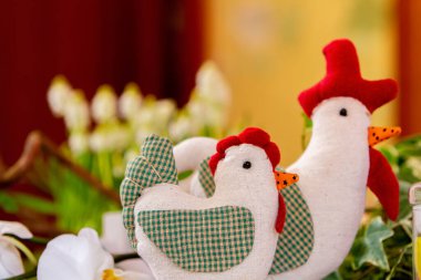 Tavuk ve horoz şeklinde iki bez bebek servis masasının üzerinde masa dekorasyonu şeklinde dururlar. Ön plandaki tavuk bebeğine odaklan..