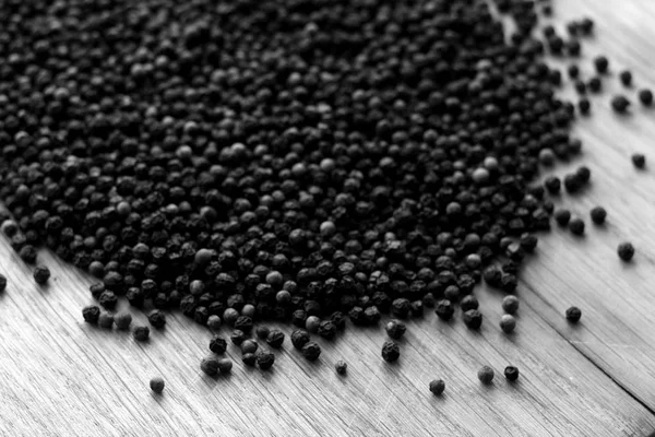 Black pepper close-up on wooden desk with blur effect in black and white. Abstract background and texture for design.