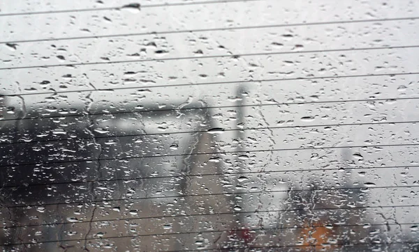 View through car rear window in rain drops with blur effect. Seasonal abstract background.