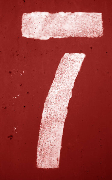 Number 7 in stencil on metal wall in red tone.