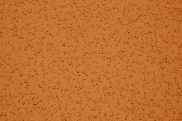Wassertropfen in orangefarbenem Ton auf Autooberfläche. — Stockfoto