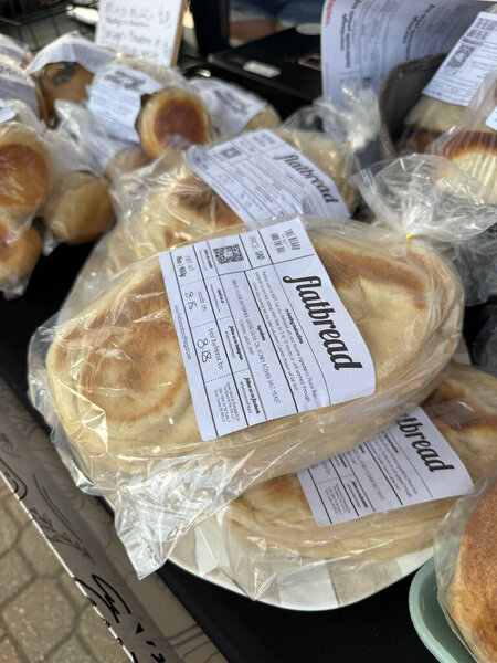 Vendors present an array of freshly baked breads at the vibrant farmers market in Holland, Michigan, attracting locals and visitors alike on a sunny day.