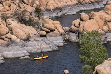İki kanocu, parlak bir günde Prescott, Arizona 'da ikonik granit kaya oluşumları tarafından kucaklanan Watson Gölü' nün sakin sularında sarı bir kano ile kürek çekiyor..