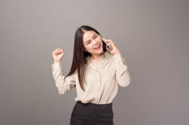 Genç güzel bir kadının portresi gri arka planda cep telefonu kullanıyor. 