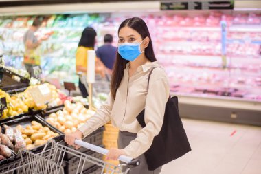 Kadın süpermarkette maskesiyle alışveriş yapıyor. 