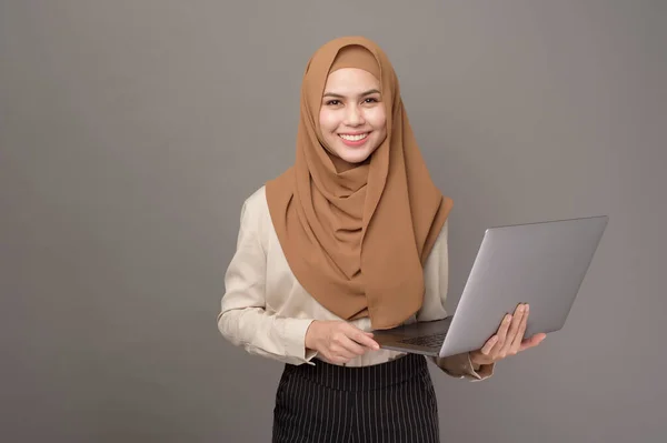 Portrait of beautiful woman with hijab is holding computer laptop on gray background