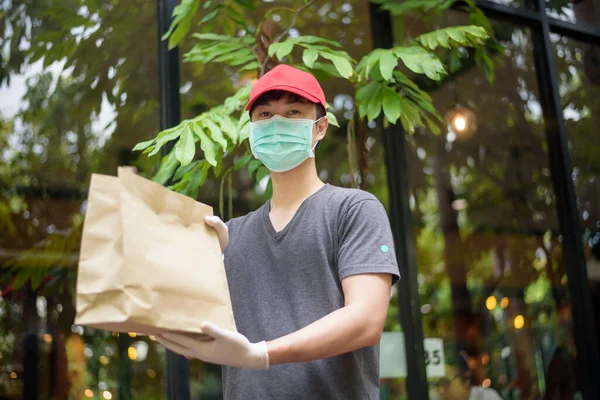 Egy Ázsiai Futár Maszkot Visel Egy Élelmiszertáskát Tart Kezében — Stock Fotó