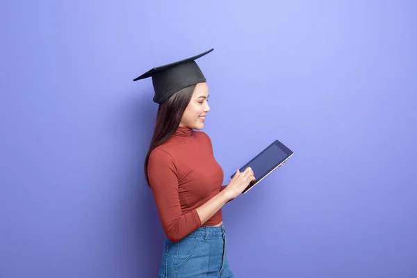 Portrait of young University student woman with graduation cap on violet background
