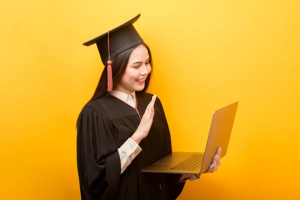 穿着毕业礼服的漂亮女人的肖像 拿着带黄色背景的笔记本电脑 — 图库照片