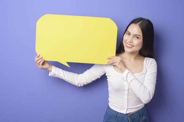 Young woman is holding yellow empty speech on purple background 