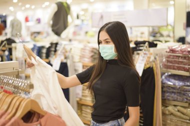 Yüzü maskeli kadın alışveriş merkezinde alışveriş yapıyor. 