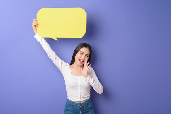 Young woman is holding yellow empty speech on purple background 