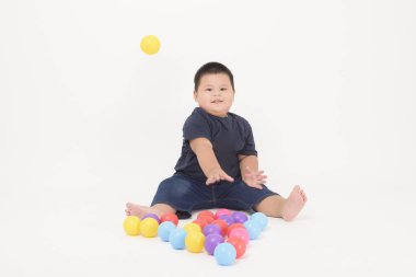 Beyaz arka plan stüdyosunda oturan ve renkli toplar oynayan sevimli küçük bir çocuğun portresi.
