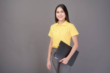 Sarı tişört giyen kendine güvenen genç bir kadın gri arka plan stüdyosunun belgelerini tutuyor.