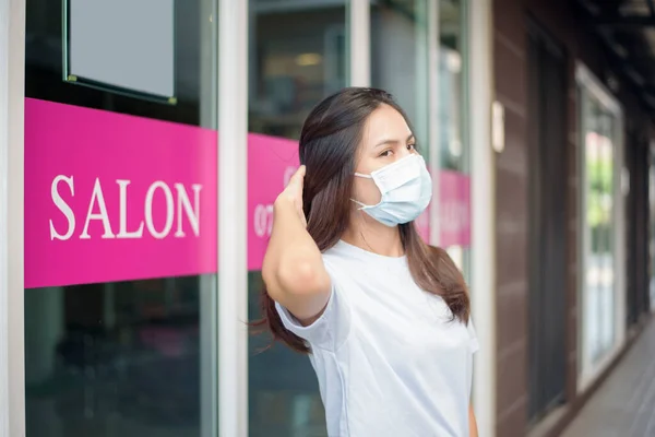 a young woman is getting a haircut in a hair salon , wearing face mask for protection covid-19 , salon safety concept