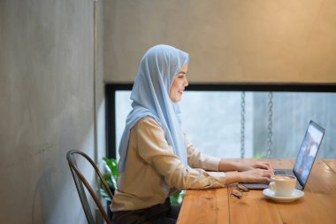 Başörtüsü olan Müslüman kadın kahve dükkanında dizüstü bilgisayarla çalışıyor.