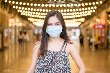 Genç bir Asyalı kadın alışveriş merkezinde koruyucu maske takıyor, Coronavirus koruması, yeni normal yaşam tarzı konsepti.
