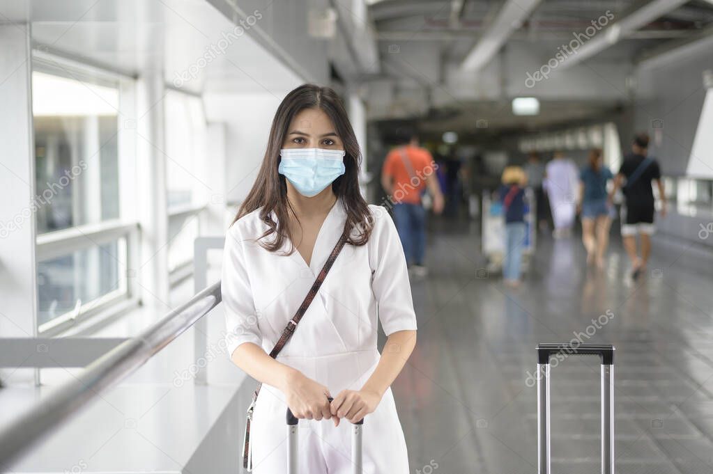A traveller woman is wearing protective mask in International airport, travel under Covid-19 pandemic, safety travels, social distancing protocol, New normal travel concept .