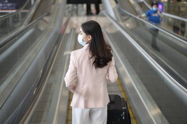 Uluslararası havaalanında koruyucu maske takan bir iş kadını Covid-19 salgını, güvenlik seyahati, sosyal mesafe protokolü, yeni normal seyahat kavramı altında seyahat ediyor..