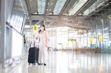 Uluslararası havaalanında koruyucu maske takan bir iş kadını Covid-19 salgını, güvenlik seyahati, sosyal mesafe protokolü, yeni normal seyahat kavramı altında seyahat ediyor..