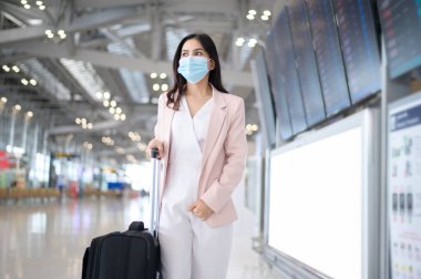 Uluslararası havaalanında koruyucu maske takan bir iş kadını Covid-19 salgını, güvenlik seyahati, sosyal mesafe protokolü, yeni normal seyahat kavramı altında seyahat ediyor..