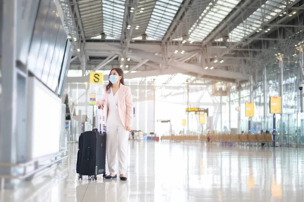 Uluslararası havaalanında koruyucu maske takan bir iş kadını Covid-19 salgını, güvenlik seyahati, sosyal mesafe protokolü, yeni normal seyahat kavramı altında seyahat ediyor..