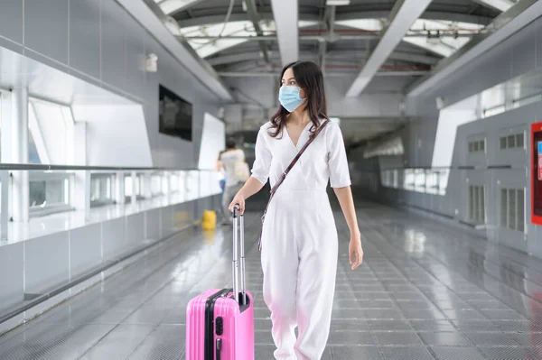 Uluslararası havaalanında koruyucu maske takan bir kadın Covid-19 salgını, güvenlik seyahati, sosyal mesafe protokolü, yeni normal seyahat kavramı altında seyahat ediyor. .