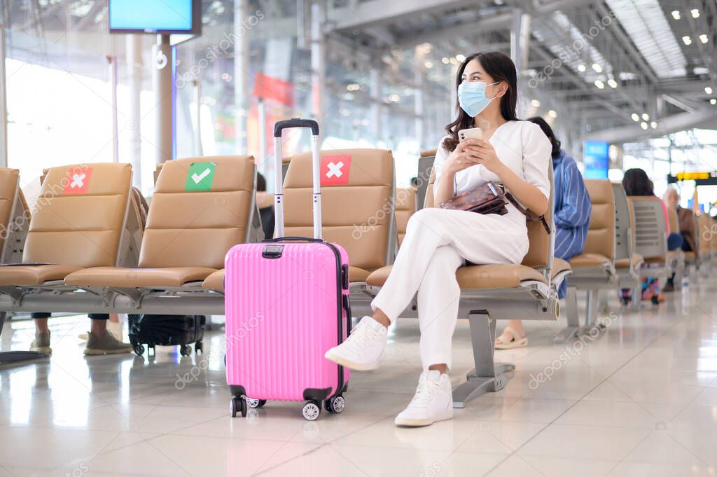 A traveller woman is wearing protective mask in International airport, travel under Covid-19 pandemic, safety travels, social distancing protocol, New normal travel concept .