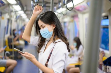Genç bir kadın metro, covid-19 koruma, güvenlik seyahati, yeni normal, sosyal uzaklık, güvenlik ulaşımı, salgın konseptiyle seyahat ederken koruyucu maske takıyor. .