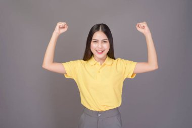 Sarı tişört giyen kendine güvenen genç bir kadın gri arka plan stüdyosunda.