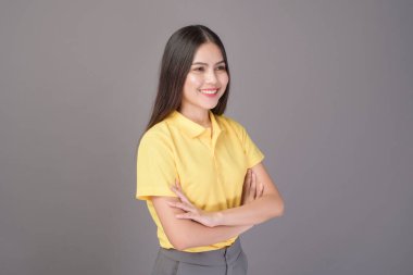 Sarı tişört giyen kendine güvenen genç bir kadın gri arka plan stüdyosunda.